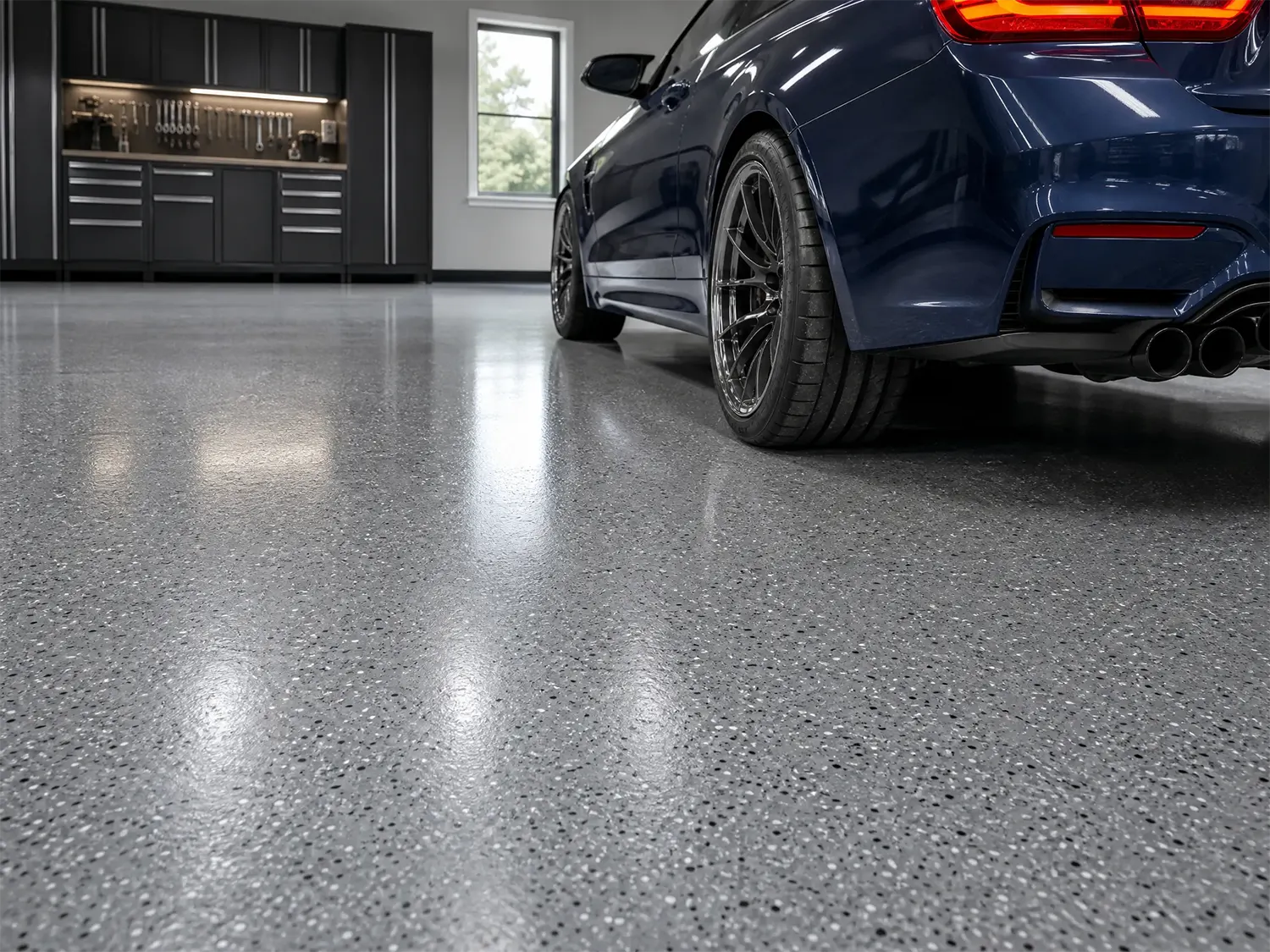 A blue car parked in a clean, modern garage with a speckled epoxy floor. In the background are cabinets, tools, and a window letting in daylight.